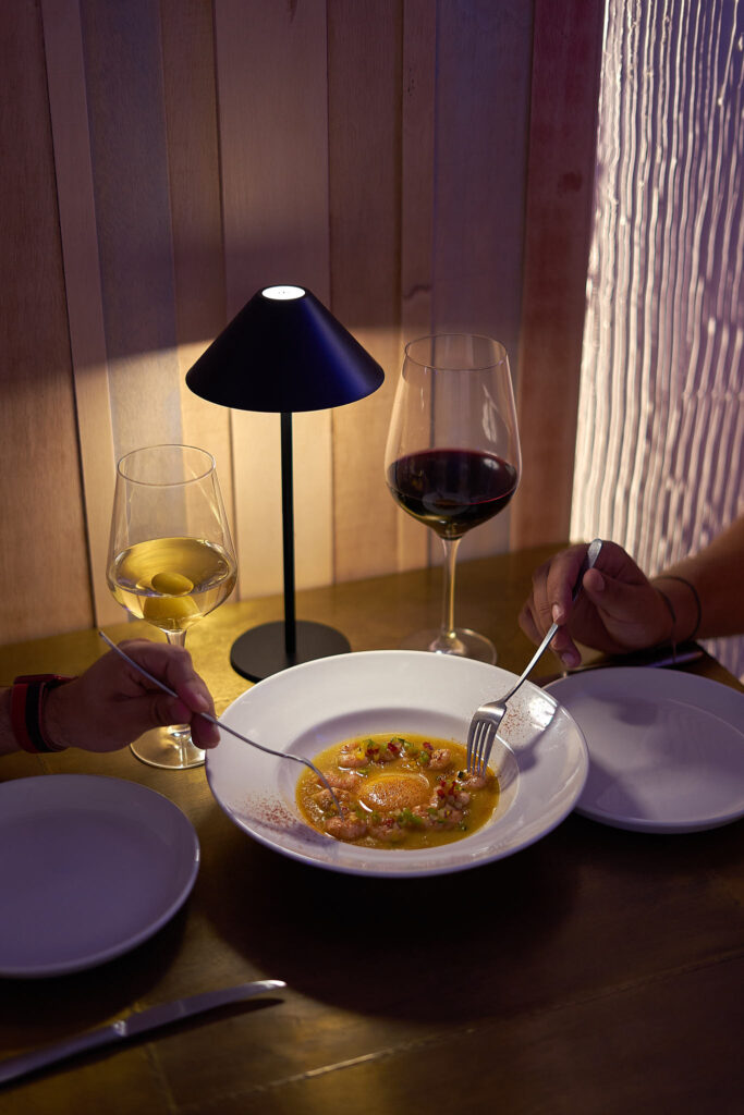Mesa de noche en Redondo en Boca con lámpara, copa de vino y un plato recién servido