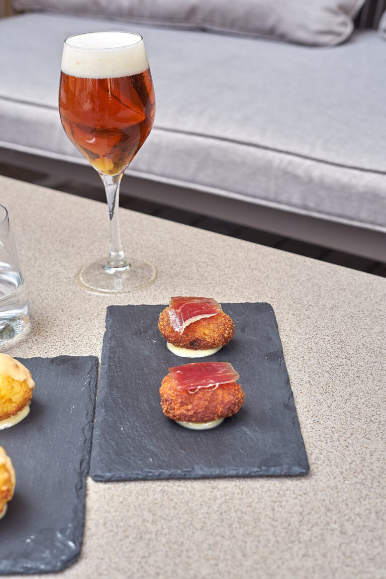 Tapas servidas sobre pizarra con una cerveza