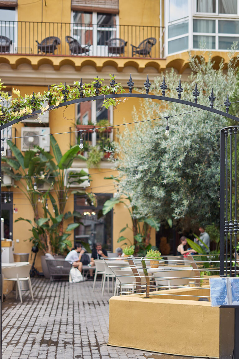 Patio interior con verja de forja, olivo y la fachada amarilla del Carmen
